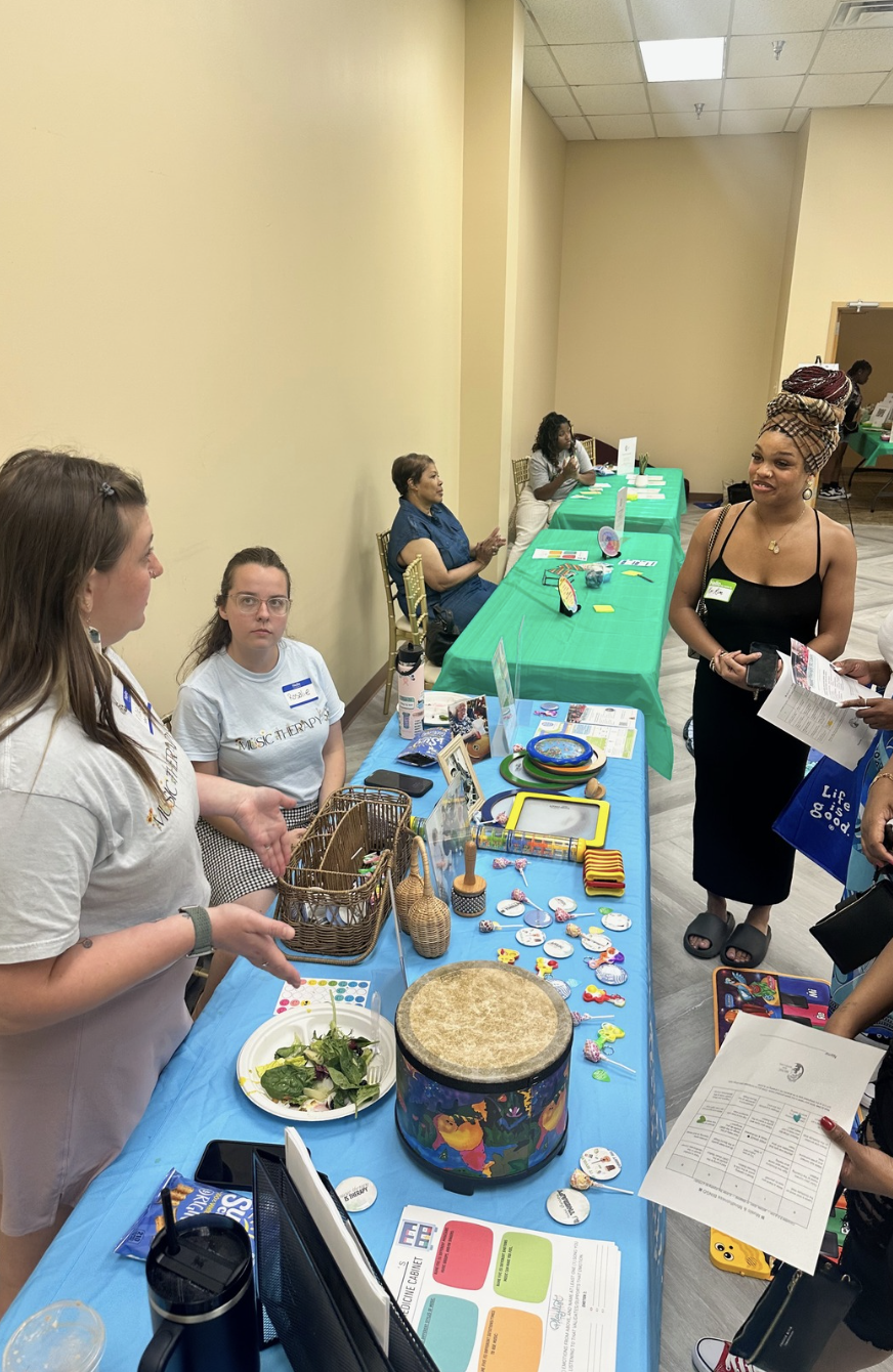 Volunteers at resource tables sharing music therapy tools with attendees